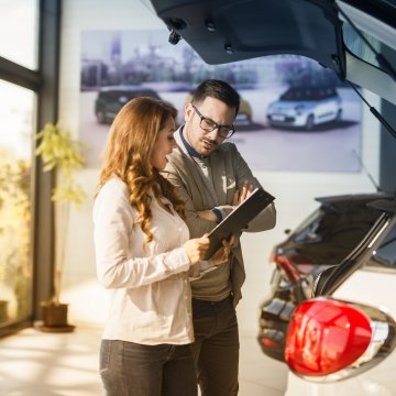 autopom! extended car warranty woman and man at car dealership signing up warranty contract cars next to them and in the background